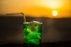 Close up wet glass of green cold mint drink, colorful orange sunset background on the terrace. Cooling summer drink. Summer fresh royalty free stock photo Close up wet glass of green cold mint drink, colorful orange sunset background on the terrace. Cooling summer drink. Summer fresh royalty free stock photo