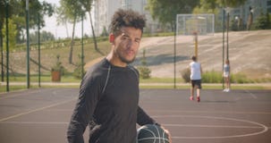 Close-upportret van jonge knappe Afrikaanse Amerikaanse mannelijke de holding van de basketbalspeler bal en in openlucht het beki stock videobeelden Close-upportret van jonge knappe Afrikaanse Amerikaanse mannelijke de holding van de basketbalspeler bal en in openlucht het beki stock videobeelden