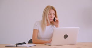 Close-upportret van volwassen Kaukasische blondeonderneemster die laptop met behulp van die een telefoongesprek binnen in het bur stock videobeelden Close-upportret van volwassen Kaukasische blondeonderneemster die laptop met behulp van die een telefoongesprek binnen in het bur stock videobeelden
