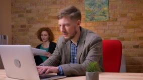 Close-upspruit van volwassen Kaukasische zakenman die aan laptop binnen in het bureau werken Onderneemster die hem behandelen stock videobeelden Close-upspruit van volwassen Kaukasische zakenman die aan laptop binnen in het bureau werken Onderneemster die hem behandelen stock videobeelden