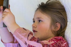 Closeup av den nätta lilla flickan i profilen som ser telefonskärmen arkivfoton Closeup av den nätta lilla flickan i profilen som ser telefonskärmen arkivfoton