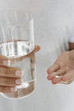 Closeup av händer som rymmer preventivpilleren och exponeringsglas av vatten royaltyfria bilder Closeup av händer som rymmer preventivpilleren och exponeringsglas av vatten royaltyfria bilder