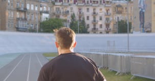 Closeup back view portrait of adult caucasian sporty male runner jogging on the stadium in the urban city outdoors stock footage Closeup back view portrait of adult caucasian sporty male runner jogging on the stadium in the urban city outdoors stock footage
