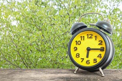 Closeup Black And Yellow Alarm Clock For Decorate Show A Quarter Past Six Or 6:15 A.m. On Old Brown Wood Desk On Green Leaves In T Stock Images