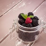 Red raspberries and blackberries in a glass jar with a leaf of mint, 1x1 size stock photography Red raspberries and blackberries in a glass jar with a leaf of mint, 1x1 size stock photography