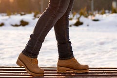 Closeup girl legs in jeans in beige boots standing on wooden bench in winter frosty sunny day on blurred background. Casual style stock image Closeup girl legs in jeans in beige boots standing on wooden bench in winter frosty sunny day on blurred background. Casual style stock image