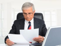 Closeup of a middle aged businessman sitting at this desk looking a documents in a modern high key office setting stock images Closeup of a middle aged businessman sitting at this desk looking a documents in a modern high key office setting stock images