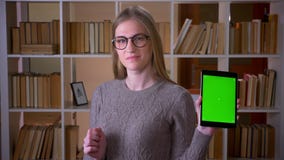 Closeup portrait of young attractive female student in glasses using the tablet and showing green screen to camera in stock video footage Closeup portrait of young attractive female student in glasses using the tablet and showing green screen to camera in stock video footage