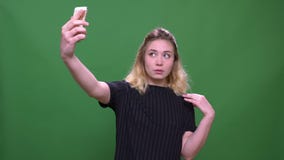 Closeup portrait of young pretty blonde caucasian female taking selfies on the phone with background isolated on green stock video footage Closeup portrait of young pretty blonde caucasian female taking selfies on the phone with background isolated on green stock video footage