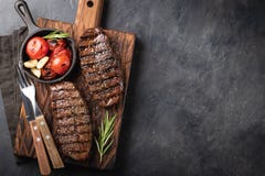 Closeup ready to eat steak Top Blade beef breeds of black Angus with grill tomato, garlic and on a wooden Board. The royalty free stock photography Closeup ready to eat steak Top Blade beef breeds of black Angus with grill tomato, garlic and on a wooden Board. The royalty free stock photography