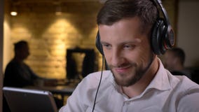 Closeup shoot of adult caucasian businessman in headphones texting on the tablet and smiling cheerfully on the workplace stock images Closeup shoot of adult caucasian businessman in headphones texting on the tablet and smiling cheerfully on the workplace stock images