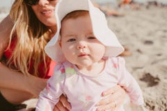 Closeup Shot Of A Caucasian Baby Girl Sitting With Her Mother On A Sandy Beach With Blur Background Stock Photo