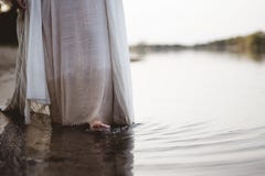 Closeup shot of a person wearing a biblical robe walking in the water near the shore