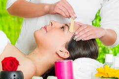Closeup womans face receiving facial hair waxing treatment, hand using wooden stick to apply wax, beauty and fashion