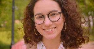 Closeupstående av den kvinnliga studenten för ung lång haired lockig caucasian i exponeringsglas som ler se lyckligt kameran lager videofilmer Closeupstående av den kvinnliga studenten för ung lång haired lockig caucasian i exponeringsglas som ler se lyckligt kameran lager videofilmer