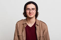Closeupstående av den tillfredsställda positiva le unga mannen som poserar över ljust - grå bakgrund, bärande beige tillfällig sk royaltyfri bild Closeupstående av den tillfredsställda positiva le unga mannen som poserar över ljust - grå bakgrund, bärande beige tillfällig sk royaltyfri bild