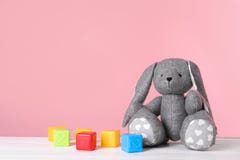Coelho adorável do brinquedo e cubos plásticos na tabela contra o fundo da cor, espaço para o texto imagem de stock royalty free Coelho adorável do brinquedo e cubos plásticos na tabela contra o fundo da cor, espaço para o texto imagem de stock royalty free