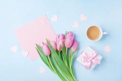 Coffee cup, spring tulip flowers, gift box and pink paper card on blue pastel table top view. Greeting for Womans or Mothers Day.