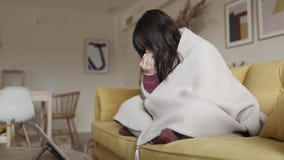 Cold young woman talking with doctor through a video call with a laptop at home