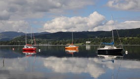 Coloured sailing boats Ullswater Lake District Cumbria England UK with mountains and blue sky on beautiful calm still day stock video footage Coloured sailing boats Ullswater Lake District Cumbria England UK with mountains and blue sky on beautiful calm still day stock video footage