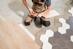 Male worker installing new wooden laminate flooring. The combination of wood panels of laminate and ceramic tiles in the stock photo Male worker installing new wooden laminate flooring. The combination of wood panels of laminate and ceramic tiles in the stock photo