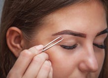 A composição mestra corrige, e dá a forma para retirar com o fórceps pintado previamente com sobrancelhas da hena em um salão de fotos de stock A composição mestra corrige, e dá a forma para retirar com o fórceps pintado previamente com sobrancelhas da hena em um salão de fotos de stock