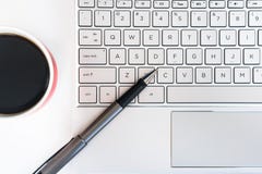 Computer portatile in bianco dello scrittorio, penna e una tazza di caffè immagini stock Computer portatile in bianco dello scrittorio, penna e una tazza di caffè immagini stock