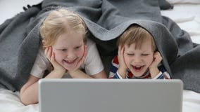 Computers in het leven van moderne kinderen weinig broer en zuster het letten op beeldverhalen op laptop, die op bed binnen ligge stock videobeelden Computers in het leven van moderne kinderen weinig broer en zuster het letten op beeldverhalen op laptop, die op bed binnen ligge stock videobeelden
