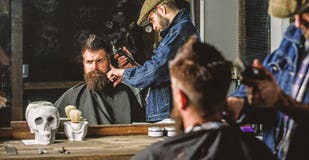 Conceito do corte de cabelo O barbeiro com tosquiadeira de cabelo trabalha no penteado para o homem com barba, fundo do barbeiro foto de stock royalty free Conceito do corte de cabelo O barbeiro com tosquiadeira de cabelo trabalha no penteado para o homem com barba, fundo do barbeiro foto de stock royalty free