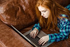 Concentrated redhead woman working with laptop and lying on couch royalty free stock photo Concentrated redhead woman working with laptop and lying on couch royalty free stock photo