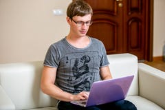 Concentrated young man with glasses working on a laptop in a home office. Type on a keyboard and scrolls text on the display stock image Concentrated young man with glasses working on a laptop in a home office. Type on a keyboard and scrolls text on the display stock image