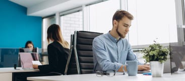 Concentrazione completa sul lavoro Giovane uomo bello della barba nel funzionamento della camicia sul computer portatile mentre s fotografie stock Concentrazione completa sul lavoro Giovane uomo bello della barba nel funzionamento della camicia sul computer portatile mentre s fotografie stock