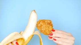 Concept de nourriture saine et malsaine banane contre la jambe de poulet pan?e frite sur un fond bleu lumineux femelle image libre de droits Concept de nourriture saine et malsaine banane contre la jambe de poulet pan?e frite sur un fond bleu lumineux femelle image libre de droits