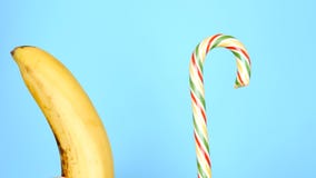 Concept de nourriture saine et malsaine banane contre la sucrerie sur un fond bleu lumineux image stock Concept de nourriture saine et malsaine banane contre la sucrerie sur un fond bleu lumineux image stock