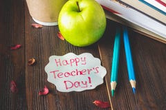 Concept of Teacher's Day. Objects on a chalkboard background. Books, green apple, plaque: Happy Teacher's Day, pencils and pens