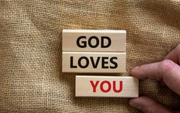 Concept words `God loves you` on wooden blocks on a beautiful canvas background, male hand. Copy space. Religion concept