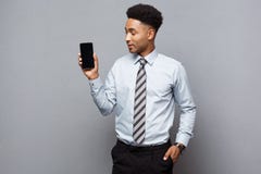 Concepto del negocio - hombre de negocios afroamericano profesional hermoso feliz que muestra el teléfono móvil al cliente Foto de archivo Concepto del negocio - hombre de negocios afroamericano profesional hermoso feliz que muestra el teléfono móvil al cliente Foto de archivo