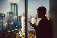 Condizione dell'uomo d'affari vicino alla finestra facendo uso del cellulare fotografie stock libere da diritti Condizione dell'uomo d'affari vicino alla finestra facendo uso del cellulare fotografie stock libere da diritti