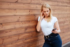 Condizione femminile di risata attraente con il telefono cellulare contro il fondo di legno della parete immagini stock libere da diritti Condizione femminile di risata attraente con il telefono cellulare contro il fondo di legno della parete immagini stock libere da diritti