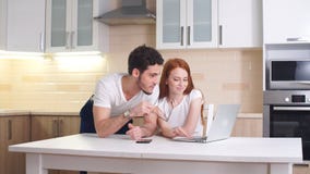 Condizione sorridente delle coppie mentre esaminando computer portatile in cucina stock footage Condizione sorridente delle coppie mentre esaminando computer portatile in cucina stock footage