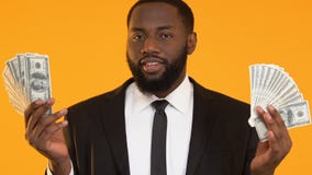 Confident black man in suit showing dollars and sending air kiss to camera