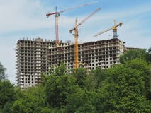 Construção de construções do multi-andar Casas e guindastes de construção no fundo do céu As árvores verdes na frente do fotos de stock Construção de construções do multi-andar Casas e guindastes de construção no fundo do céu As árvores verdes na frente do fotos de stock
