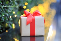 Contenitore di regalo con il nastro rosso su luce dorata con il BAC dell'estratto del bokeh immagine stock Contenitore di regalo con il nastro rosso su luce dorata con il BAC dell'estratto del bokeh immagine stock