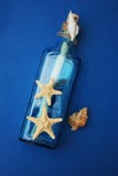 Contexto náutico do tema, garrafa decorativa com shell, estrela do mar no fundo do azul de Depp Copie o espaço Foco seletivo fotografia de stock Contexto náutico do tema, garrafa decorativa com shell, estrela do mar no fundo do azul de Depp Copie o espaço Foco seletivo fotografia de stock