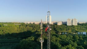 Contractor working on telecommunications mast at height on background of beautiful city landscape, drone view of