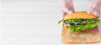 Cook`s Hands Lay A Herring Fillet Sandwich With Onions, Cucumber And Salad On Paper. White Wooden Background With Copy Space For Stock Photos