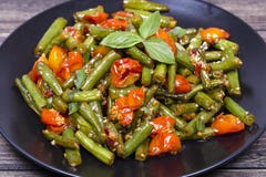 Cooked green beans, red cherry tomato with sesame seeds in black plate. Close up Stock Photos Cooked green beans, red cherry tomato with sesame seeds in black plate. Close up Stock Photos