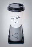 Copo de papel preto e branco para o café com o trabalho da inscrição posto sobre um telefone preto foto de stock Copo de papel preto e branco para o café com o trabalho da inscrição posto sobre um telefone preto foto de stock