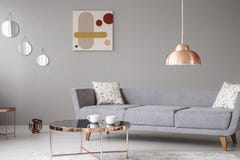 Copper lamp and coffee table in front of a modern sofa in a grey living room interior