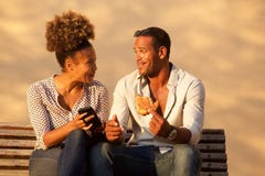 Coppia la seduta sul banco di parco con il telefono cellulare e lo spuntino immagine stock libera da diritti Coppia la seduta sul banco di parco con il telefono cellulare e lo spuntino immagine stock libera da diritti